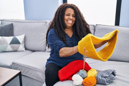 Photo for African american woman sitting on sofa sewing handmade clothes at home - Royalty Free Image