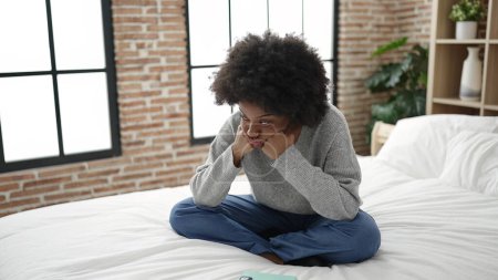 Téléchargez les photos : Femme afro-américaine couchée sur le lit avec une expression ennuyeuse dans la chambre - en image libre de droit