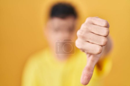 Téléchargez les photos : Homme hispanique portant des lunettes debout sur fond jaune regardant malheureux et en colère montrant rejet et négatif avec les pouces vers le bas geste. mauvaise expression. - en image libre de droit