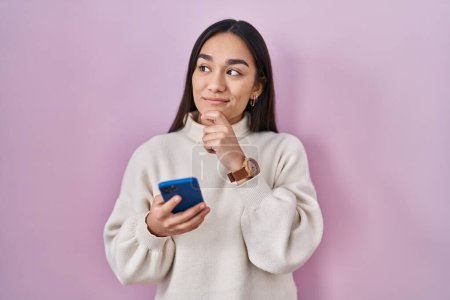 Photo for Young south asian woman using smartphone serious face thinking about question with hand on chin, thoughtful about confusing idea - Royalty Free Image