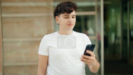 Téléchargez les photos : Non binary man using smartphone with relaxed expression at street - en image libre de droit