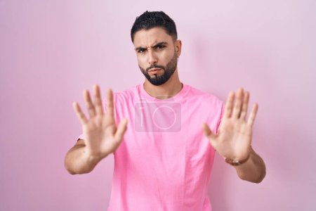 Photo for Hispanic young man standing over pink background moving away hands palms showing refusal and denial with afraid and disgusting expression. stop and forbidden. - Royalty Free Image