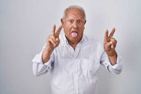 Téléchargez les photos : Senior man with grey hair standing over isolated background smiling with tongue out showing fingers of both hands doing victory sign. number two. - en image libre de droit