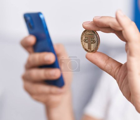 Hombre de mediana edad que sostiene la moneda criptográfica mediante el teléfono inteligente en casa