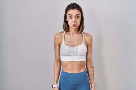 Photo for Hispanic woman wearing sportswear over isolated background puffing cheeks with funny face. mouth inflated with air, crazy expression. - Royalty Free Image