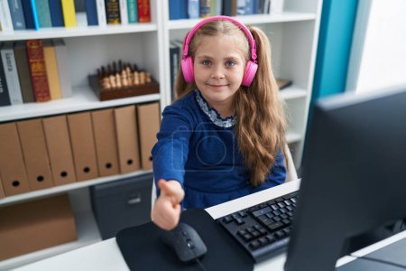 Foto de Adorable estudiante rubia chica usando la computadora y los auriculares haciendo el gesto de pulgar hacia arriba en el aula - Imagen libre de derechos
