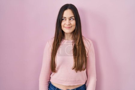 Foto de Young brunette woman standing over pink background smiling looking to the side and staring away thinking. - Imagen libre de derechos