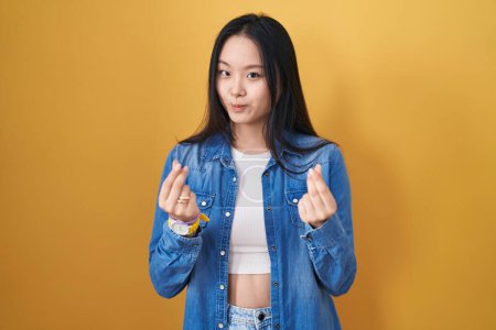 Téléchargez les photos : Jeune femme asiatique debout sur fond jaune faisant geste d'argent avec les mains, demandant le paiement du salaire, entreprise millionnaire - en image libre de droit
