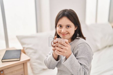 Téléchargez les photos : Jeune femme avec le syndrome du duvet boire une tasse de café assis sur le lit dans la chambre - en image libre de droit