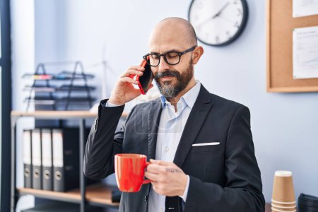 Téléchargez les photos : Jeune homme chauve homme d'affaires parlant sur smartphone boire du café au bureau - en image libre de droit