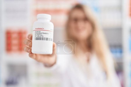 Foto de Joven mujer farmacéutica sosteniendo pastillas botella en la farmacia - Imagen libre de derechos