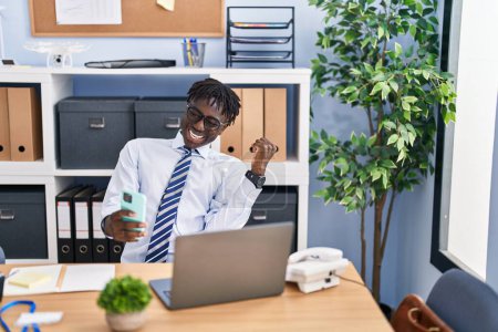 Téléchargez les photos : Homme d'affaires afro-américain utilisant un smartphone avec expression gagnante au bureau - en image libre de droit