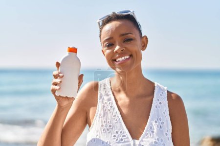 Photo for African american woman smiling confident holding sunscreen bottle at seaside - Royalty Free Image