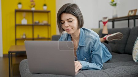 Foto de Mujer caucásica joven usando el ordenador portátil tumbado en el sofá en casa - Imagen libre de derechos