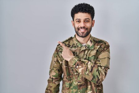 Photo for Arab man wearing camouflage army uniform cheerful with a smile on face pointing with hand and finger up to the side with happy and natural expression - Royalty Free Image