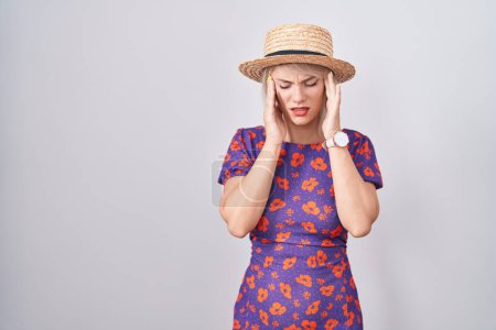 Foto de Mujer caucásica joven con vestido de flores y sombrero de verano con la mano en la cabeza, dolor de cabeza porque el estrés. padecer migraña. - Imagen libre de derechos
