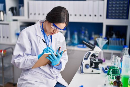 Photo for Young woman scientist writing on notebook at laboratory - Royalty Free Image