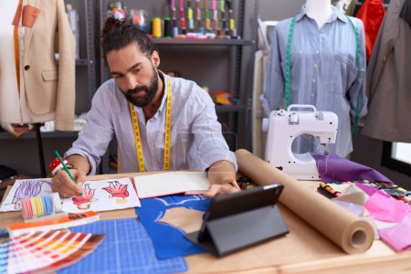 Téléchargez les photos : Young hispanic man tailor drawing clothing design using touchpad at atelier - en image libre de droit