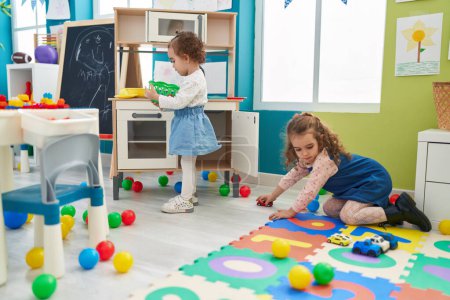 Téléchargez les photos : Adorables filles jouant avec la cuisine de jeu et jouet de voiture à la maternelle - en image libre de droit