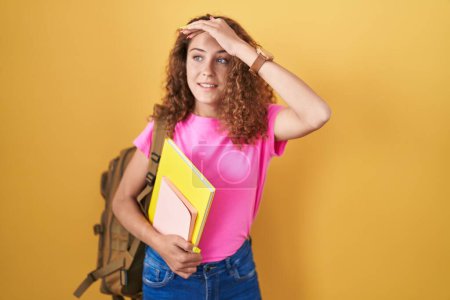 Photo for Young caucasian woman wearing student backpack and holding books very happy and smiling looking far away with hand over head. searching concept. - Royalty Free Image