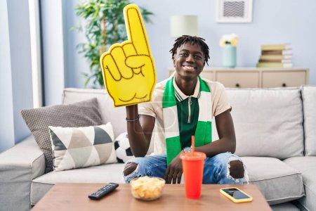Photo for African man with dreadlocks football hooligan supporting team looking positive and happy standing and smiling with a confident smile showing teeth - Royalty Free Image