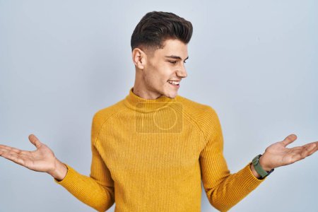 Photo for Young hispanic man standing over blue background smiling showing both hands open palms, presenting and advertising comparison and balance - Royalty Free Image