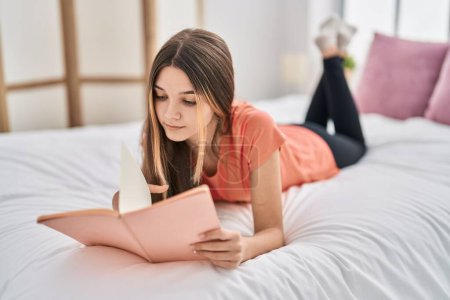 Foto de Adorable chica leyendo libro acostado en la cama en el dormitorio - Imagen libre de derechos