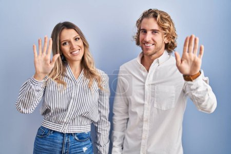 Téléchargez les photos : Jeune couple debout sur fond bleu renonçant à dire bonjour heureux et souriant, geste de bienvenue amical - en image libre de droit