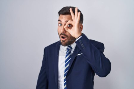 Photo for Handsome hispanic man wearing suit and tie doing ok gesture shocked with surprised face, eye looking through fingers. unbelieving expression. - Royalty Free Image