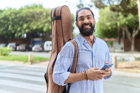 Téléchargez les photos : Young hispanic man musician using smartphone holding guitar case at street - en image libre de droit