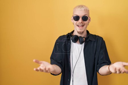 Photo for Young caucasian man wearing sunglasses standing over yellow background smiling cheerful offering hands giving assistance and acceptance. - Royalty Free Image
