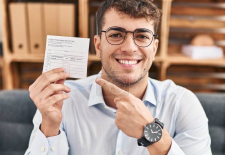 Téléchargez les photos : Jeune homme hispanique tenant une carte de disque covid souriant heureux pointant avec la main et le doigt - en image libre de droit