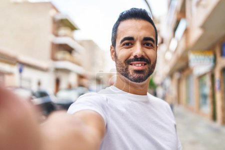 Foto de Joven hombre hispano sonriendo confiado haciendo selfie por la cámara en la calle - Imagen libre de derechos
