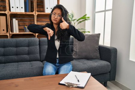 Foto de Mujer asiática joven en la oficina de consulta haciendo pulgares arriba y abajo, el desacuerdo y la expresión de acuerdo. conflicto loco - Imagen libre de derechos
