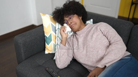 Foto de Joven afroamericana mujer viendo la televisión acostada en el sofá en casa - Imagen libre de derechos
