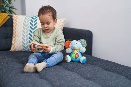 Téléchargez les photos : Adorable garçon hispanique jouant avec jouet assis sur le canapé à la maison - en image libre de droit