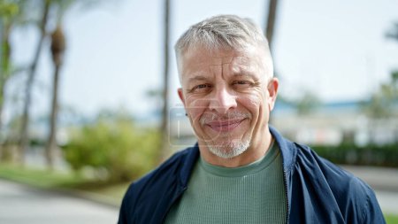 Téléchargez les photos : Homme aux cheveux gris d'âge moyen souriant confiant debout au parc - en image libre de droit