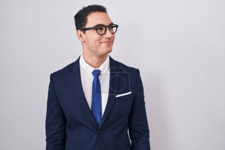 Téléchargez les photos : Jeune homme hispanique portant costume et cravate souriant regardant vers le côté et regardant loin en pensant. - en image libre de droit