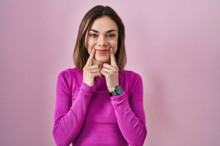 Téléchargez les photos : Hispanic woman standing over pink background smiling with open mouth, fingers pointing and forcing cheerful smile - en image libre de droit