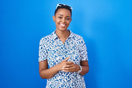 Téléchargez les photos : Femme afro-américaine debout sur fond bleu avec les mains jointes et les doigts croisés souriant détendu et joyeux. succès et optimisme - en image libre de droit