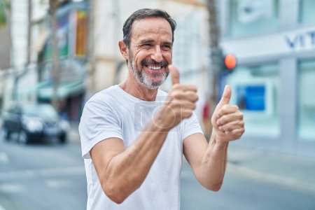 Téléchargez les photos : Moyen Age homme souriant confiant faire ok signe avec les pouces dans la rue - en image libre de droit