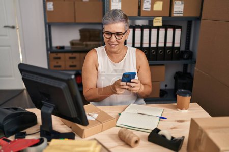 Foto de Middle age woman ecommerce business worker using smartphone at office - Imagen libre de derechos
