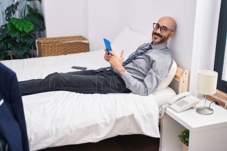 Photo for Young hispanic man business worker using touchpad lying on bed at hotel room - Royalty Free Image