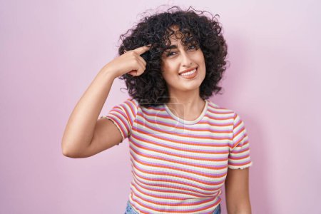 Téléchargez les photos : Jeune femme du Moyen-Orient debout sur fond rose souriant pointant vers la tête avec un doigt, bonne idée ou pensée, bonne mémoire - en image libre de droit