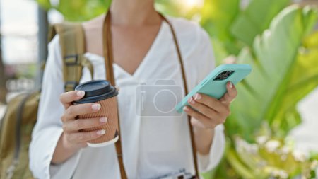 Foto de Joven hermosa turista hispana usando smartphone bebiendo café en el parque - Imagen libre de derechos