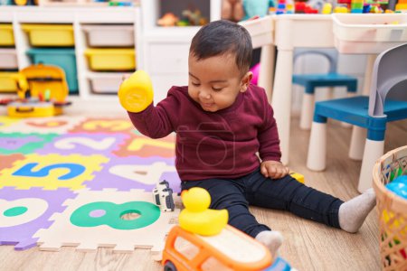 Photo for Adorable hispanic boy playing with duck toy sitting on floor at kindergarten - Royalty Free Image