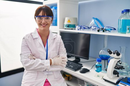 Foto de Joven morena trabajando en laboratorio científico cara feliz sonriendo con los brazos cruzados mirando a la cámara. persona positiva. - Imagen libre de derechos