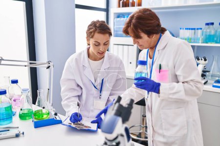 Photo for Two women scientists holding test tube writing on document at laboratory - Royalty Free Image