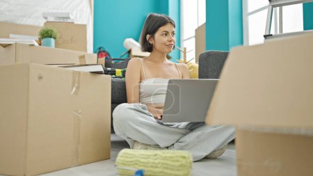 Téléchargez les photos : Jeune belle femme hispanique utilisant un ordinateur portable assis sur le sol à la nouvelle maison - en image libre de droit