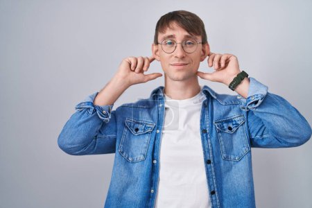 Photo for Caucasian blond man standing wearing glasses covering ears with fingers with annoyed expression for the noise of loud music. deaf concept. - Royalty Free Image
